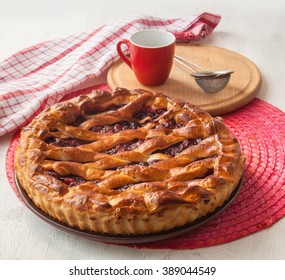 Open cherry pie on the red stand next to a sieve to sprinkle powdered sugar