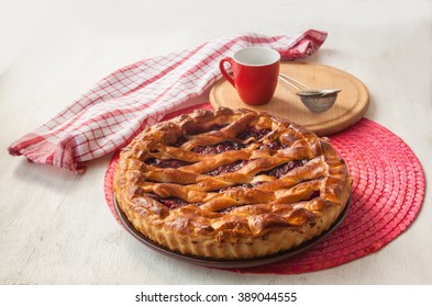 Open cherry pie on the red stand next to a sieve to sprinkle powdered sugar
