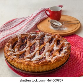 Open cherry pie on the red stand next to a sieve to sprinkle powdered sugar