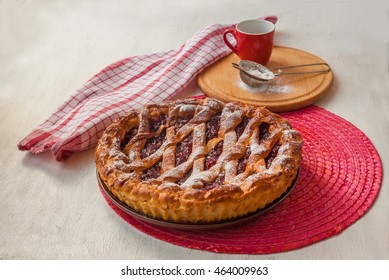 Open cherry pie on the red stand next to a sieve to sprinkle powdered sugar