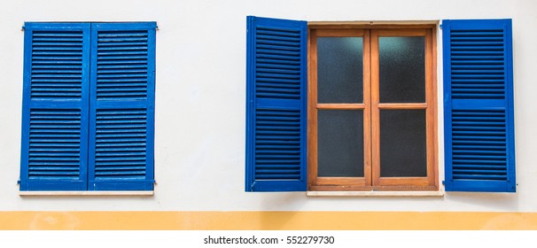 Open And Closed Blue Painted Wood Window Shades With Yellow Line Wall Color On The Bottom And Half-transparent Glass Windows With Brown Colored Wood.