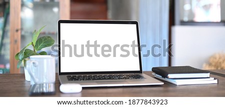 An open computer laptop, coffee cup, notebook and plant on wooden table. Blank screen monitor for graphic display montage.