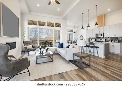 open concept living room with stylish furniture electric fireplace grey leather arm chairs windows revealing blue sky hardwood floors and view to kitchen - Powered by Shutterstock