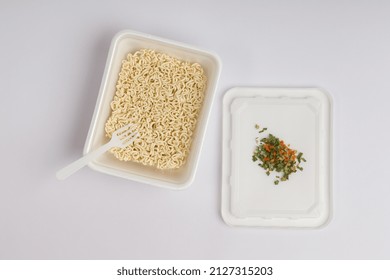 Open Container With Instant Noodles With A Plastic Fork And Dry Vegetables On A White Background. Fast Food Concept