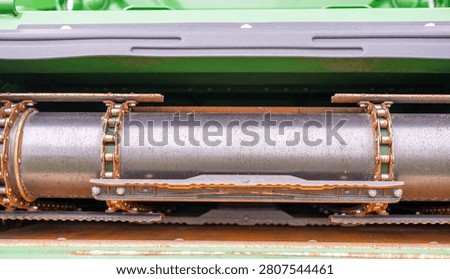 Open conveyor system of a combine tractor showing rust with visible mechanical parts and structure near a farm field
