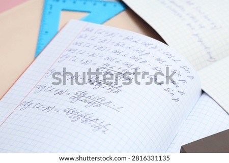 Open copybook with maths formulas and ruler on color table, closeup