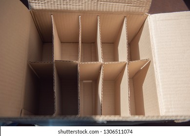 An Open Corrugated Brown Cardboard Box Showing Dividers And Nothing Inside. A Box Placed On The Wooden Floor With Sun Light.