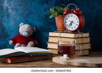 Open Diary, Cup of Hot Tea, Books, Red Alarm Clock on a dark blue background. School concept.