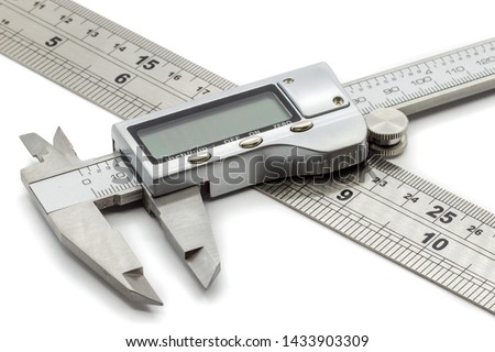 Open digital vernier calipers rest on top of a metal ruler that displays inches and centimetres on a white background