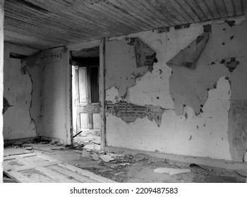 An Open Dilapidated And Peeling Door Viewed Through A Another Door Frame From Inside Of An Old Abandoned Room With Peeling Paint Crumbling Plaster And Warped Floor Boards