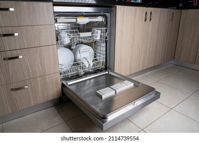 Open door of built-in dishwasher. Kitchen with integrated appliances. Plates and dishes in the dishwasher. Integration of household appliances in a modern kitchen.