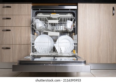 Open door of built-in dishwasher. Kitchen with integrated appliances. Plates and dishes in the dishwasher.