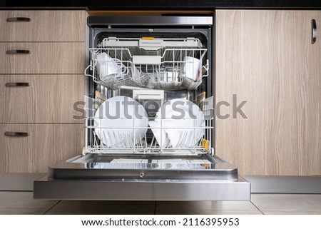 Open door of built-in dishwasher. Kitchen with integrated appliances. Plates and dishes in the dishwasher. Foto d'archivio © 