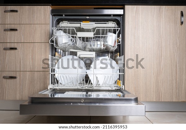 Open door of\
built-in dishwasher. Kitchen with integrated appliances. Plates and\
dishes in the dishwasher.