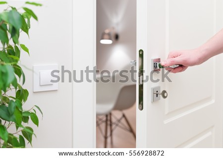 To open the door. Modern white door with chrome metal handle and a man's arm. Elements of interior closeup