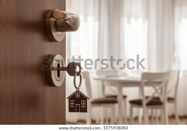 Open door to a new home. Door handle with key and\
home shaped keychain. Mortgage, investment, real estate, property\
and new home concept