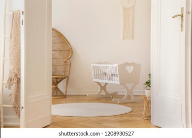 Open Door To White Scandi Kid Room With Cradle And Wicker Peacock And Carpet On The Parquet, Real Photo