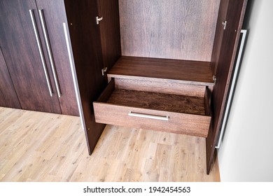 Open Doors And Drawer Of Elegant Wardrobe Made Of Dark Oak Veneer With Shiny Metal Handles In Minimal Style In Room Closeup