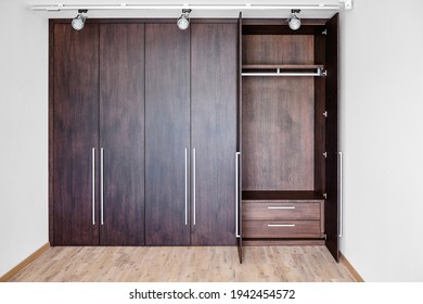 Open doors of elegant wardrobe with inner drawer made of dark oak veneer with shiny metal handles in minimal style in room - Shutterstock ID 1942454572