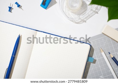 Open dotted notebook with blue pen, pencils, eraser, ruler, tape, sharpener, pins. Workspace background, copyspace.