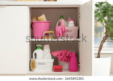 Open drawer with baskets of different cleaning supplies, brushes, pink rubber gloves and sponges in kitchen