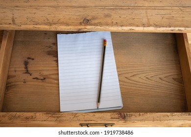 Open drawer with notepad and pencil in old wooden table
