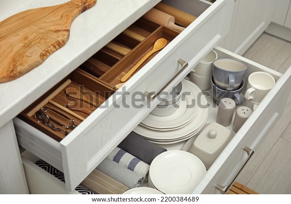 Open drawers of kitchen cabinet with different\
dishware, utensils and\
towels