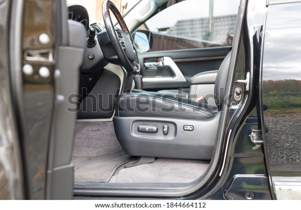 Open driver\'s door\
overlooking the front row of passenger armchair upholstered in\
black leather of a clean sedan interior with a view of the seat\
adjustment buttons.