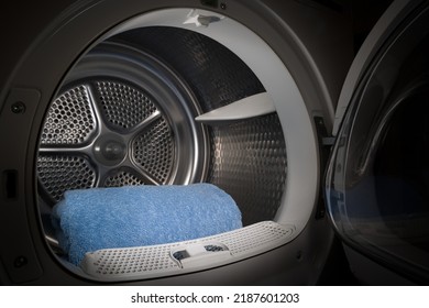 Open dryer with blue towels inside. Washing machine in a dark room.