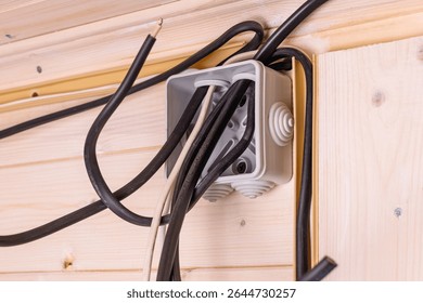 Open electrical junction box with multiple black and white wires protruding in wooden wall, showing installation stage and safety importance.