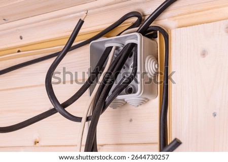 Open electrical junction box with multiple black and white wires protruding in wooden wall, showing installation stage and safety importance.