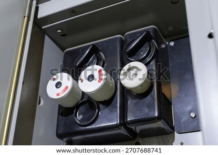 An open electrical panel reveals multiple ceramic fuses and fuse holders, some labeled L10A, indicating their amperage within an industrial setting.