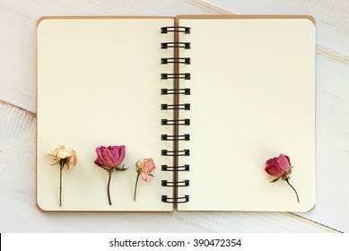 Open empty copy book with dried roses. Blank creamy pages.