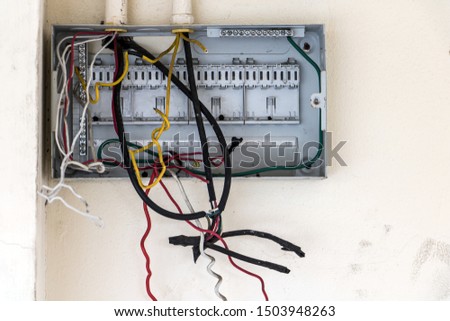 A open empty electricity fuse box with cables on white wall. Electrical control panel with empty fuse boxes inside an abandoned building. Damaged circuit breaker.