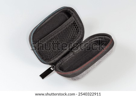 Open empty small plastic hard case with gray textile covering, inside mesh pocket and zipper for different accessories storing on a gray background