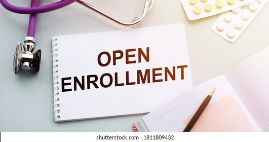 OPEN ENROLLMENT text written in a notebook lying on a medicine desk and a stethoscope. Medical concept.