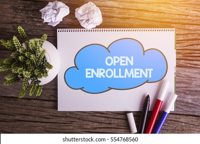 OPEN ENROLLMENT word with Notepad and green plant on wooden background
