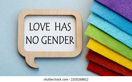 An open envelope with the words LOVE HAS NO GENDER rests on a stack of fabric folded in the colors of the LGBT flag. Flat lay, top view. LGBT concept.