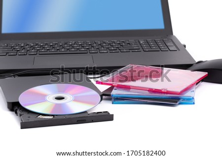 an open external computer DVD CD drive with a pile of CD cases and a notebook computer in the background