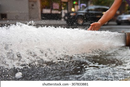 Open fire hydrant/child's hand touching water as it flows vigorously from opened fire hydrant in city street