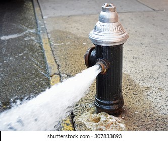 Open fire hydrant/water flowing vigorously from open fire hydrant on city street and sidewalk