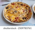 An open or flat omelette with tomatoes, mushrooms, onions and cheese, served on a plate.