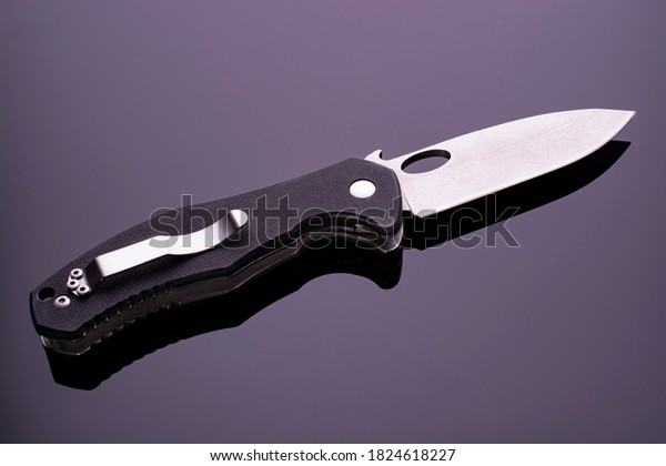 open
folding pocket knife with textured black composite plastic cover
plates on steel handle isolated on dark background with reflection
on glossy surface. Pocket knife close-up
image