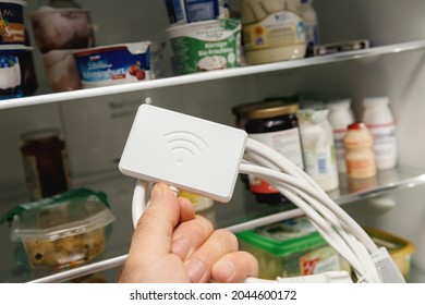 Open Fridge Door With Male Hand Holding New Wifi Dongle For Modern Refrigerators With New Fridge In Background - Control With App And Smartphone