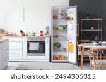 Open fridge full of fresh food near white wall in kitchen