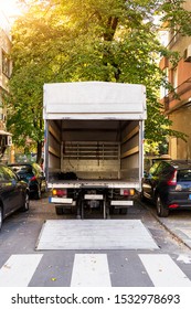 Open Furniture Delivery Truck On A City Street. Empty Moving Van With Rear Doors Opened. On An Autumn Sunny Day. Back View.