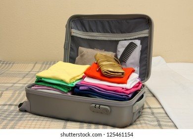 Open Grey Suitcase With Clothing On Bed