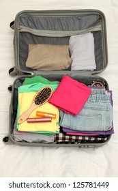 Open Grey Suitcase With Clothing On Bed