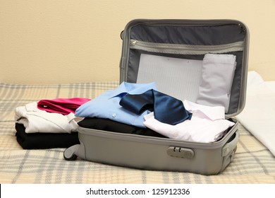 Open Grey Suitcase With Clothing On Bed