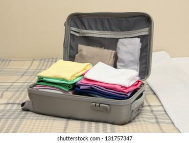 Open Grey Suitcase With Clothing On Bed